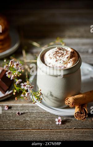 Mexikanische heiße Schokolade mit Schlagsahne auf dunklem Holzhintergrund mit Blumen, Keksen und Zimtstangen. Stockfoto