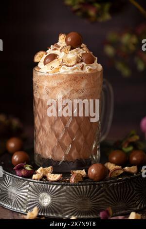 Eine heiße Schokolade in einem alten Glasbecher mit Schlagsahne und Schokoladenkugeln aus Honeycombe. Stockfoto