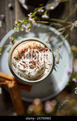 Mexikanische heiße Schokolade mit Schlagsahne auf dunklem Holzhintergrund mit Blumen, Keksen und Zimtstangen. Stockfoto