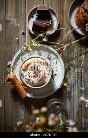 Mexikanische heiße Schokolade mit Schlagsahne auf dunklem Holzhintergrund mit Blumen, Keksen und Zimtstangen. Stockfoto