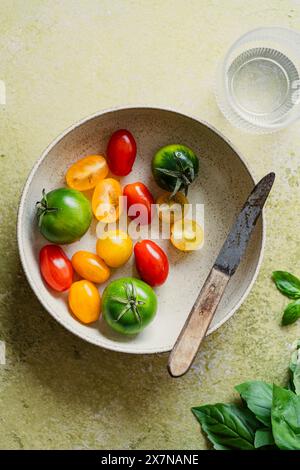 Schüssel mit kleinen, farbigen charry und Pflaumentomaten mit einem kleinen Messer auf grünem Hintergrund Stockfoto