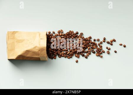 Kaffeebohnen, die aus dem Papierbeutel auf einen einfachen Hintergrund gegossen werden. Stockfoto