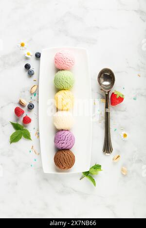 Set aus verschiedenen Eislöffeln und Beeren auf weißem Marmorhintergrund. Erdbeere, Pistazien, Mango, Vanille, Heidelbeere und Schokoladeneis. Oben Stockfoto