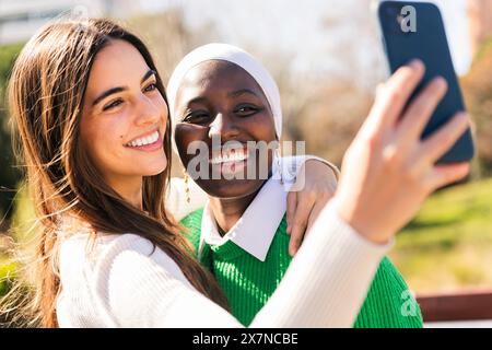 Zwei junge Freundinnen lächeln glücklich, während sie Selfie-Fotos mit dem Handy machen, Freundschaftskonzept und moderner Lebensstil Stockfoto