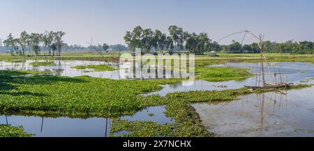 Landschaftlich reizvolle Landschaft mit Holzbooten und traditionellen chinesischen Fischernetzen in Tangail Country, Bangladesch Stockfoto