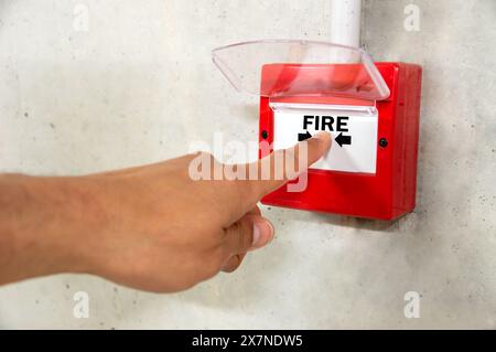 Nahaufnahme der männlichen Hand, die auf den roten Feueralarm-Schalter an der Betonwand im Bürogebäude zeigt. Ausrüstung des industriellen Brandwarnsystems für den Notfall. Stockfoto