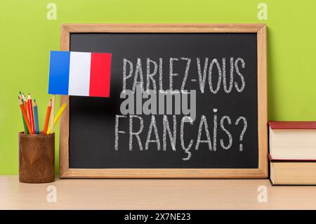 Eine Tafel mit der Frage parlez-vous francais? Sprichst du französisch? Auf französisch geschrieben, ein Topf mit Bleistiften und die Fahne Frankreichs, auf einem hölzernen de Stockfoto