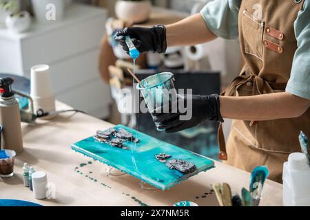Die Künstlerin gießt Epoxidharz und schmiert es mit einem Stock auf Holzbrett, mit Hilfe von Flüssigkunsttechnik Stockfoto
