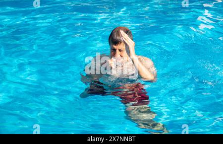 Ein Mann mit einem schmerzenden Kopf von der Sonne, die im Wasser eines Pools oder Spas schwimmt. Blasen Sie auf den Kopf, wenn Sie in den Pool springen Stockfoto