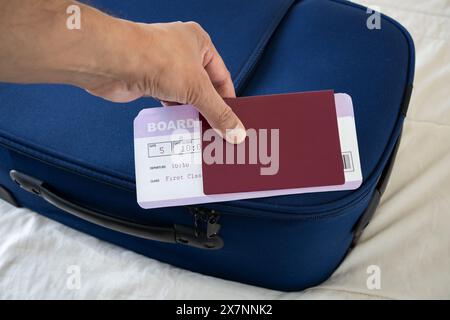 Nicht erkennbarer Geschäftsmann zeigt Reisepass und Flugticket auf einem blauen Koffer auf einem Bett Stockfoto