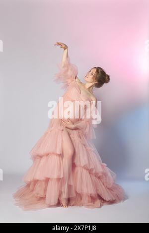 Eine anmutige schwangere Frau steht in einem Studio und trägt ein pinkfarbenes Kleid Stockfoto