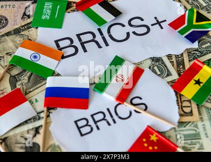 Die Wörter und Länderflaggen einiger Länder des BRICS- und BRICS+-Blocks auf einem Stapel von US-Dollar-Scheinen. Ein Demoollarisierungskonzept. Stockfoto