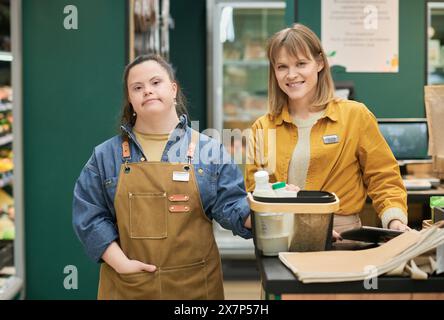 Porträt eines lächelnden Managers und einer jungen Frau mit Down-Syndrom, die im Supermarkt arbeitet und die Kamera zusammen posiert Stockfoto