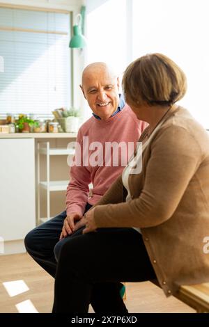 Senior Pärchen sitzen zusammen in einer Küche und führen ein freundliches Gespräch. Ein älteres Paar teilt einen Moment der Freude und Zuneigung. Stockfoto