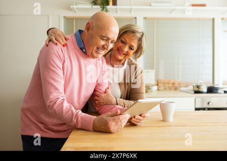 Seniorenpaar in einer Küche, die glücklich zusammen ein Tablet ansieht. Stockfoto