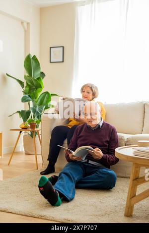 Ein älteres Ehepaar liest zusammen Bücher im Wohnzimmer. Senior-Mann sitzt auf dem Boden, während seine Frau auf dem Sofa sitzt und beide A lesen Stockfoto