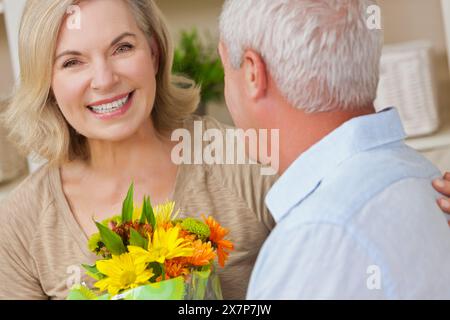 Glückliche ältere Frau, die romantische Blumen empfängt, ältere Mann und Frau Paar zu Hause lächelnd und gesund Stockfoto