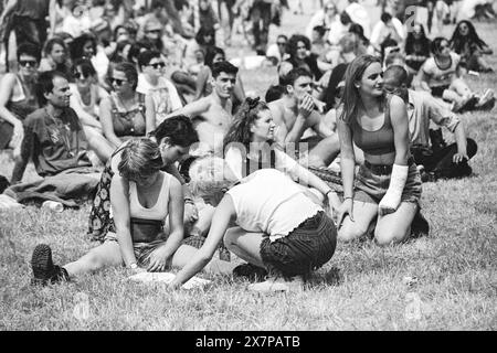 FESTIVALPROGRAMM, CROWD, HEATWAVE, NME STAGE, GLASTONBURY 95: Festivalbesucher krachen auf dem Gras ab und sehen sich das Line-up im Festivalprogramm in der extremen Sommer Heatwave auf dem zweiten NME Stage Field und Crowd beim Glastonbury Festival, Pilton Farm, Somerset, England, 24. Juni 1995 an. 1995 feierte das Festival sein 25-jähriges Bestehen. Viele Menschen hatten an dem besonders heißen Wochenende Probleme mit dem Hitzschlag. Foto: ROB WATKINS Stockfoto