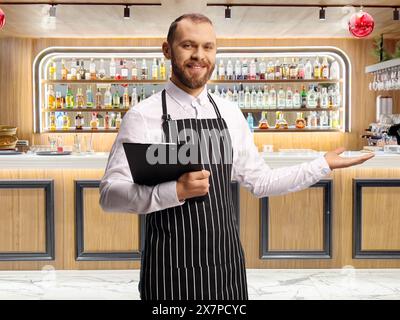 Kellner, der ein Menü hält und an einer Bar willkommen geheißen wird Stockfoto