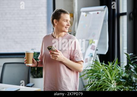 Eine professionelle Frau, die mit einer Kaffeetasse und einem Handy multitaskt. Stockfoto