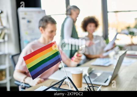 Konzentrieren Sie sich auf die Regenbogenfahne, die auf dem Bürotisch vor verschwommenen Geschäftsfrauen zu sehen ist. Stockfoto