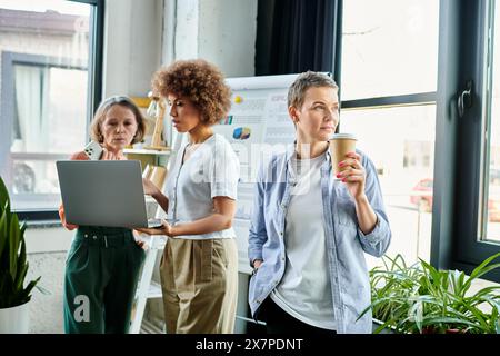 Verschiedene Gruppen von Geschäftsfrauen versammelten sich um einen Laptop in einem gemeinsamen Arbeitsbereich. Stockfoto