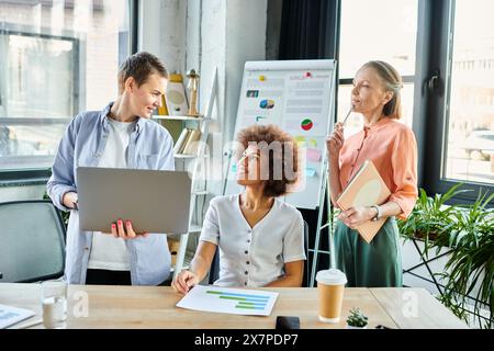 In einem modernen Büro versammelten sich verschiedene weibliche Profis an einem Tisch mit einem Laptop. Stockfoto