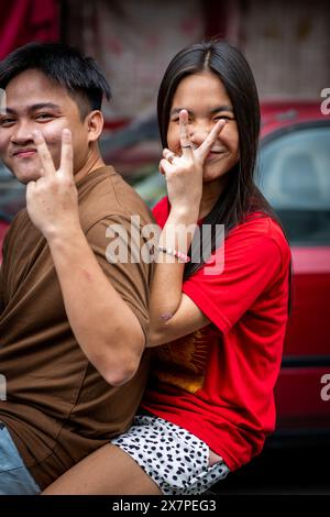 Ein junges philippinisches Paar rastet auf einem Roller vorbei und macht lustige Handsignale im Tondo District Manila auf den Philippinen. Stockfoto