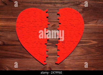 Gebrochenes rotes Puzzle in Herzform auf hölzernem Hintergrund. Verlorene Liebe, zerrüttete Beziehungen und die Hoffnung auf Heilung und Verbindung. Stockfoto