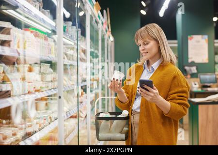 Seitliches Porträt einer erwachsenen Frau, die ihr Smartphone benutzt, während sie im Supermarkt einkaufen Stockfoto