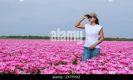 Eine Frau steht anmutig in einem Feld aus leuchtenden rosa Tulpen, umgeben von Naturschönheiten in Texel, Niederlande. Stockfoto