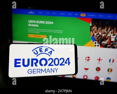 Person mit Smartphone und Logo der Fußball-Europameisterschaft UEFA Euro 2024 vor der Website. Schwerpunkt auf dem Display des Telefons. Stockfoto