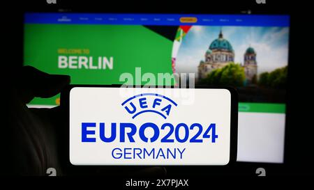 Person mit Handy mit Logo der Fußball-Europameisterschaft UEFA Euro 2024 vor der Webseite. Schwerpunkt auf dem Display des Telefons. Stockfoto