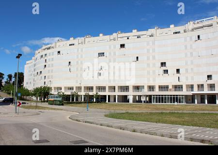 Großes kurviges, neu gebautes, modernes, weißes, städtisches Apartmentgebäude mit offenen und geschlossenen Fensterläden auf der sonnigen Straßenseite mit einer Reihe von Plastik Stockfoto