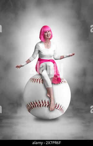 Porträt einer jungen Frau mit rosa Haaren, die auf einem riesigen Baseball sitzt Stockfoto