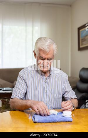 Ein älterer Mann misst sorgfältig seinen Blutzuckerspiegel an einem Tisch in seinem Haus und zeigt, wie wichtig die Überwachung des Blutzuckers für die Behandlung von Hypoglykämie ist Stockfoto