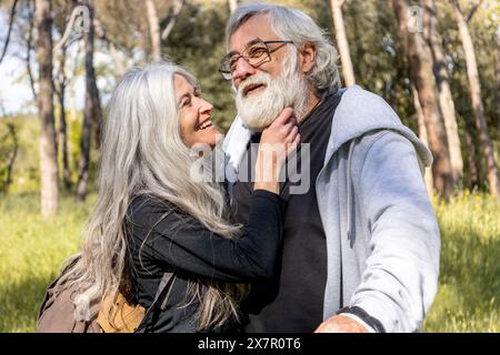 Ein älterer Mann und eine ältere Frau umarmen sich freudig in einem sonnendurchfluteten Park und zeigen Zuneigung und Glück in ihren goldenen Jahren, ein echtes Lächeln und eine ungezwungene Atmosphäre Stockfoto