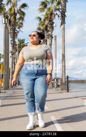 Eine selbstbewusste Frau genießt an einem warmen Sommertag einen gemütlichen Spaziergang zwischen Barcelonas berühmten Palmen und verkörpert den entspannten urbanen Lebensstil Stockfoto