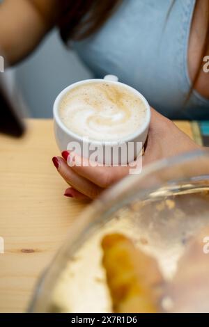 Nahaufnahme einer Frau, die eine Tasse Cappuccino neben einem Kuchenteig hält, was eine entspannende Pause während der Kuchenzubereitung symbolisiert Stockfoto