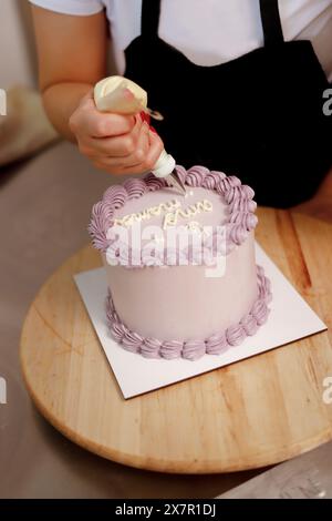 Ein Bäcker dekoriert einen Kuchen mit einem Gebäckbeutel und fügt der glatten mattierten Oberfläche elegante Schriftzüge hinzu Stockfoto