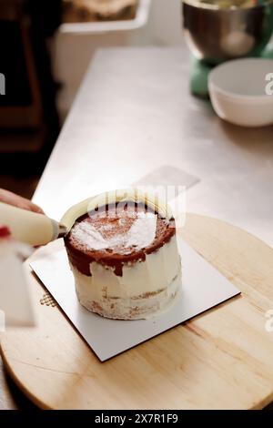 Ein Konditor dekoriert einen frisch gebackenen Kuchen mit weißem Puderzucker mit einem Paspelbeutel auf einer Küchenarbeitsfläche, der die Kunst der Kuchenherstellung widerspiegelt Stockfoto