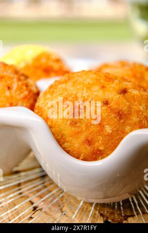 Ein köstlicher Blick aus nächster Nähe auf goldbraune Arancini, traditionelle italienische Reisbällchen, serviert in einer weißen Keramikschale auf einem rustikalen Hintergrund Stockfoto