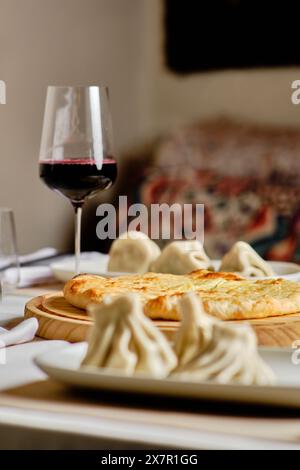 Ein traditionelles georgianisches fest mit Khachapuri und hinkali, perfekt kombiniert mit einem Glas Rotwein, vor einem sanft verschwommenen Hintergrund Stockfoto