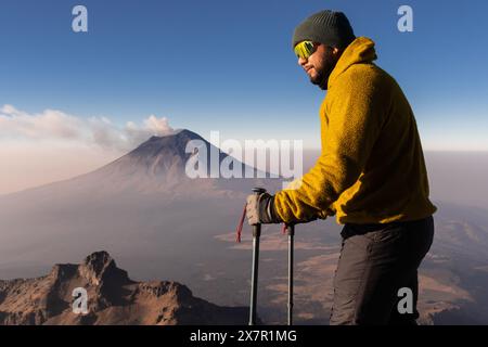 Ein Wanderer in gelbem Fleece hält an den Hängen von Iztaccíhuatl an und beobachtet an klaren Tagen den rauchenden Vulkan Popocatépetl Stockfoto