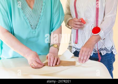 Zwei Personen arbeiten in einer Nähwerkstatt zusammen, einer markiert den Stoff, während der andere ein Kissen hält, um Zusammenarbeit und Handwerkskunst in GA zu demonstrieren Stockfoto