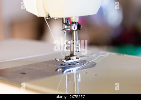 Ein Nahbild der Nadel und des Nähfußes einer Nähmaschine, das die Details der Nähausrüstung in einer Designwerkstatt erfasst Stockfoto