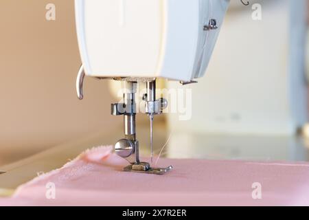 Eine detaillierte Nahaufnahme der Nadel und des Fußes einer Nähmaschine mit rosafarbenem Stoff, die die Präzision der Bekleidungsherstellung in einer Designwerkstatt veranschaulicht Stockfoto