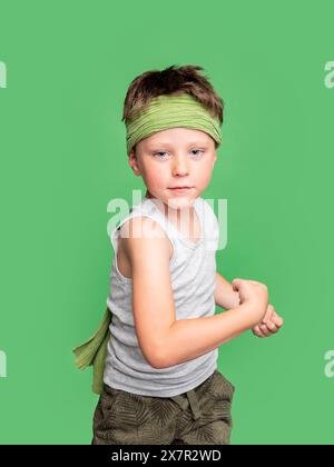 Junge mit einem ernsten Ausdruck, der ein Stirnband trägt, posiert in einem Studio mit grünem Hintergrund und blickt in die Kamera. Stockfoto
