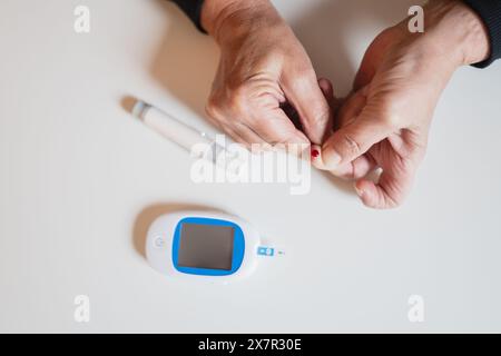 Eine ältere Person, die den Blutzuckerspiegel mit einem Bluttropfen an der Fingerspitze und einem digitalen Blutzuckermessgerät testet, die das häusliche Diabetesmanagement und Moni veranschaulicht Stockfoto