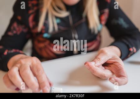 Eine Frau mittleren Alters führt zu Hause einen Blutzuckertest durch, eine wichtige Aktivität zur Überwachung und Behandlung von Hypoglykämien Stockfoto